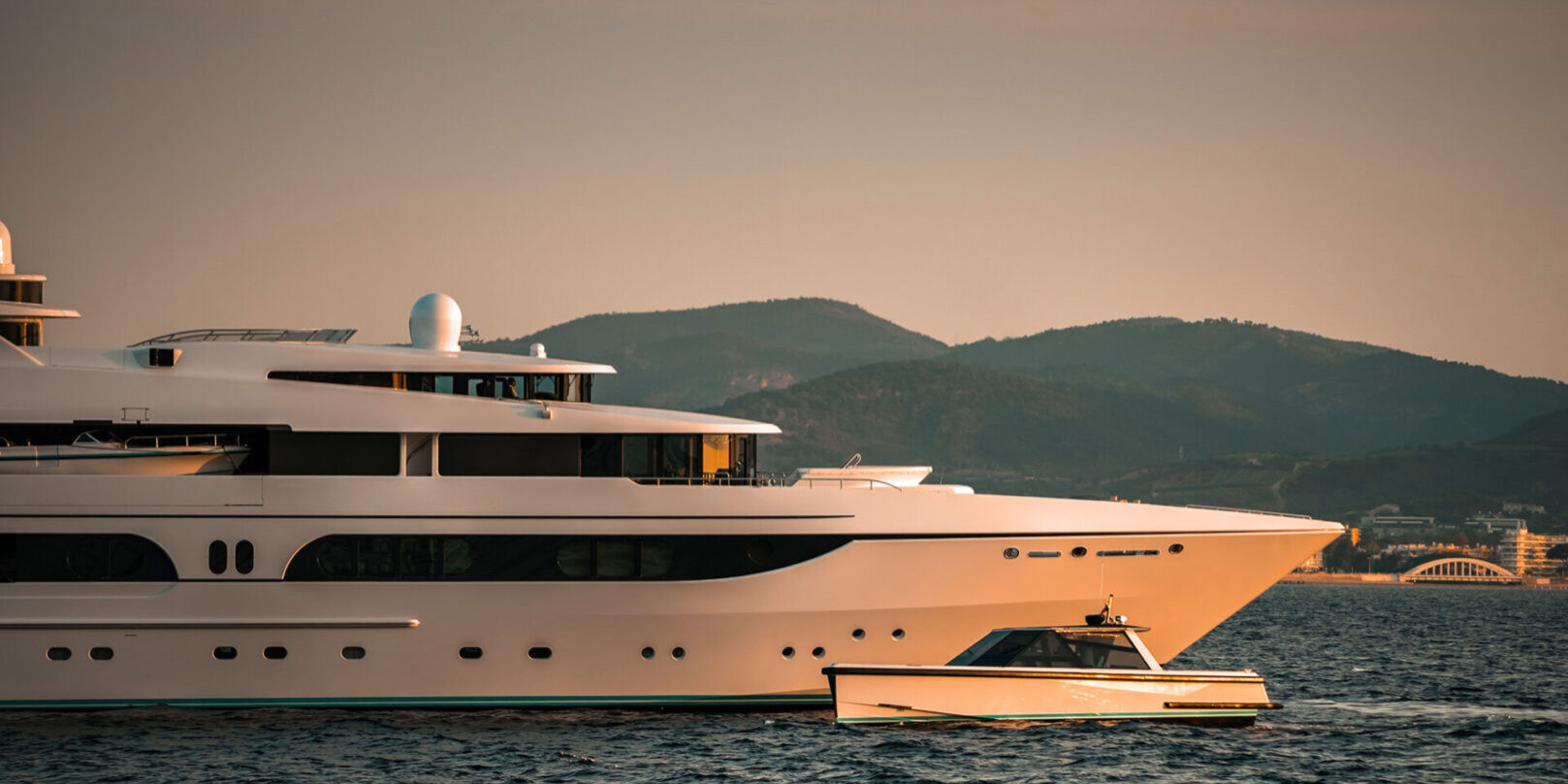 Mood detail shot of Superyacht bow with it's tender chase boat motoring past on a sunset warm light in the bay of Saint-Tropez, South of France